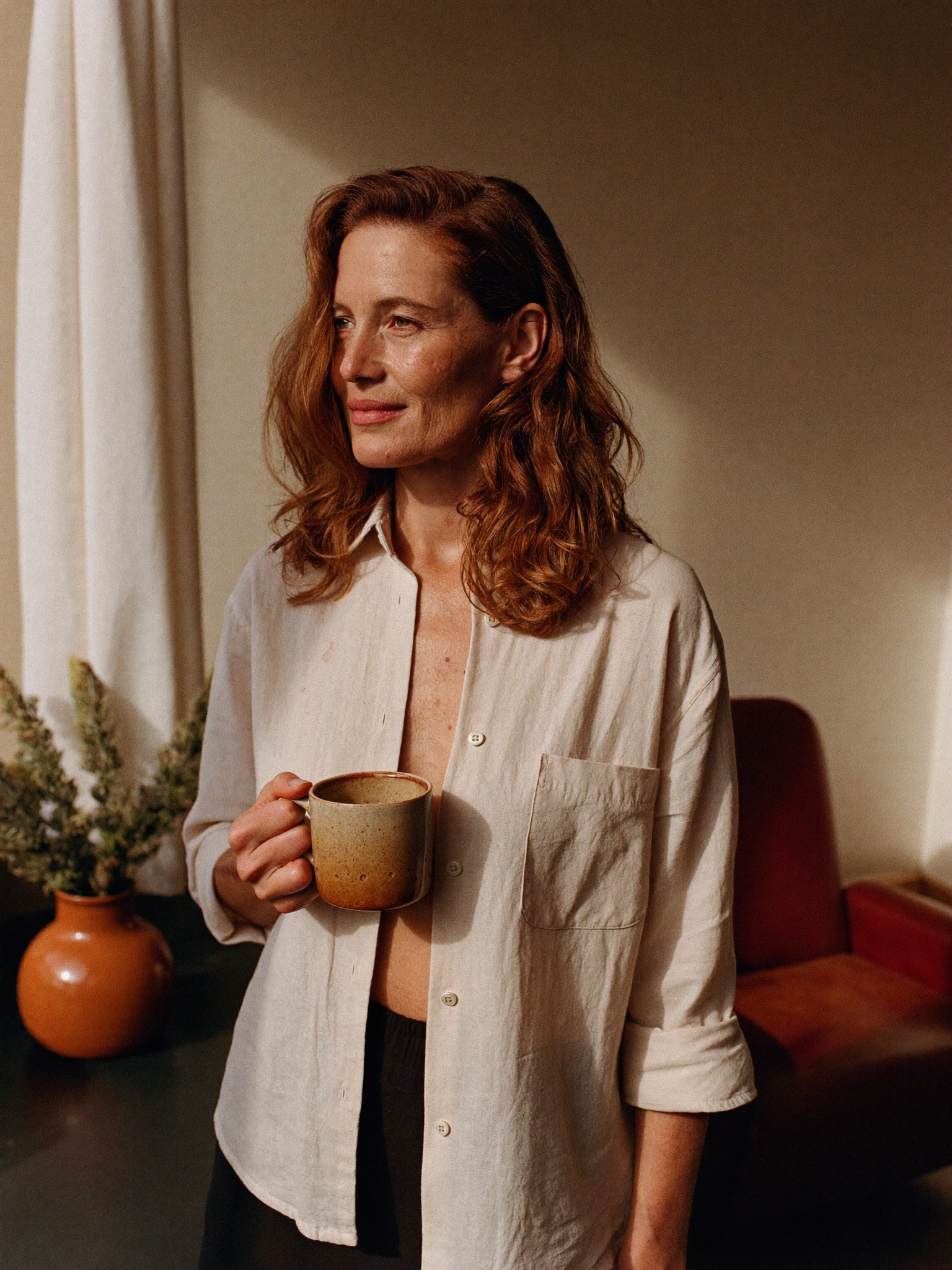 MenoReign hero — confident woman in warm sunlit interior with terracotta and oxblood accents